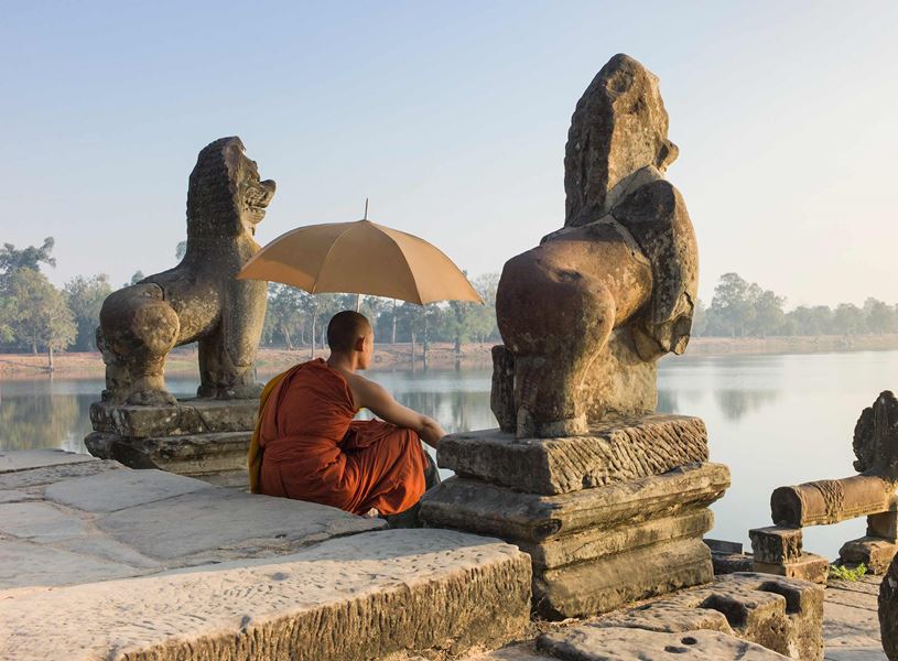 Buddhist monk sitting by water at sunrise, Sra Srong, Angkor Wat, Cambodia
