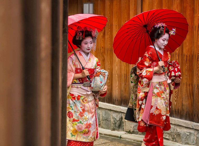 Two Maiko women with red umbrellas walking in Kyoto, Japan