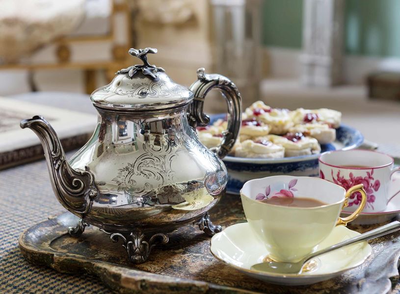 Silver teapot on tray with cups and saucers and scones in London, England