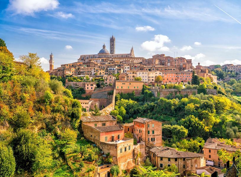 Panoramic view of Siena in Tuscany with buildings, cathedral dome and green hill