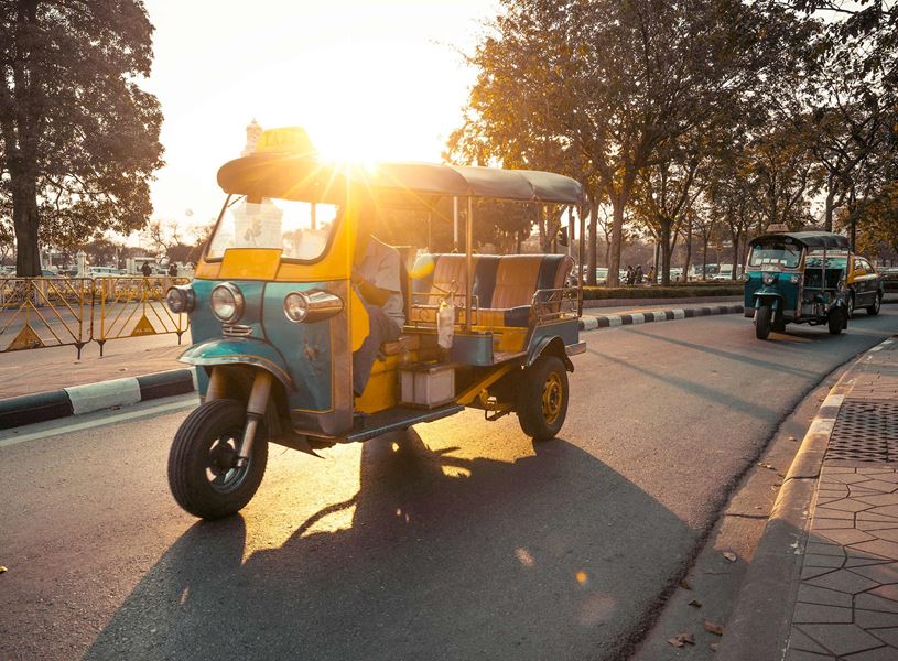 Tuk-tuk driving on sunlit street with trees in Bangkok, Thailand