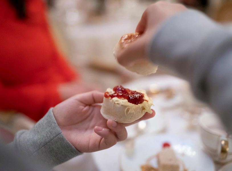 Hands assembling scone with clotted cream and jam in Devon, England