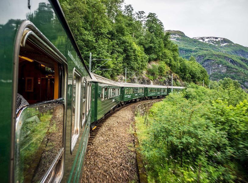 Green Flåm Railway train winding through valley with mountains in Norway