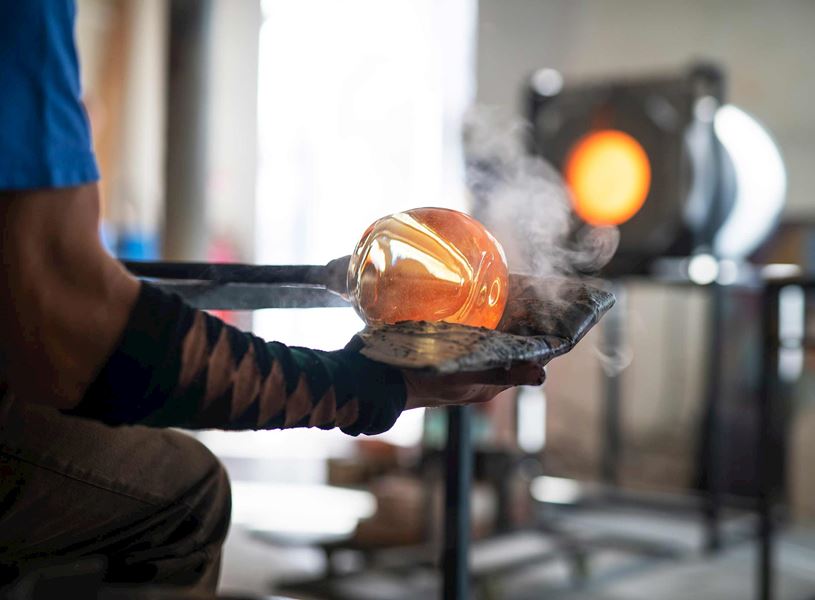 Glassblower shaping molten glass sphere with metal tools 