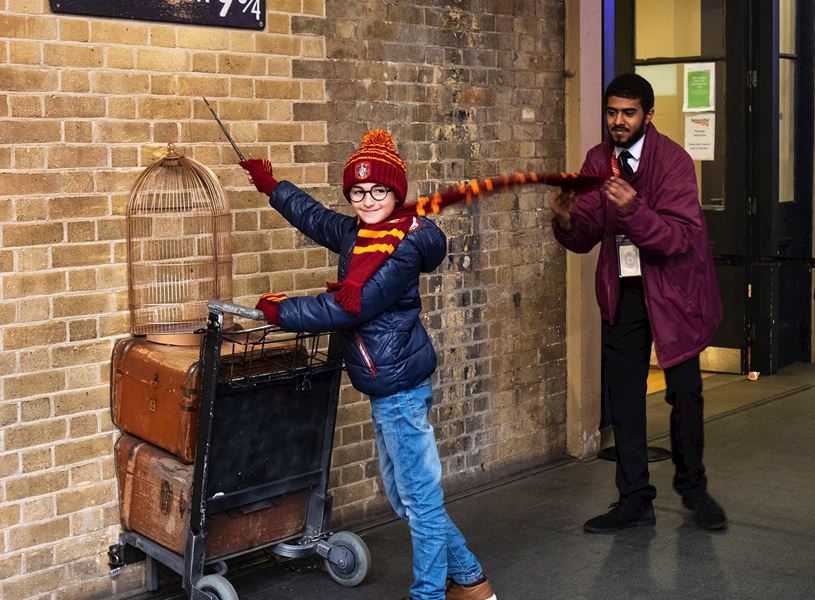Person posing at Harry Potter Platform 9 and ¾ with luggage cart in London