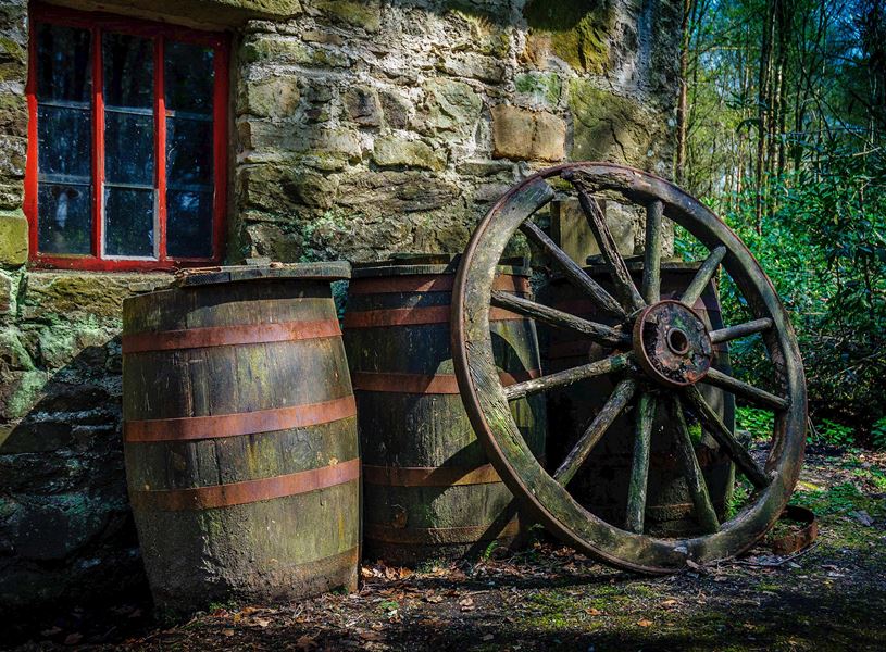 Two wooden barrels and rustic wagon wheel outside stone cottage at Ulster American Folk Park