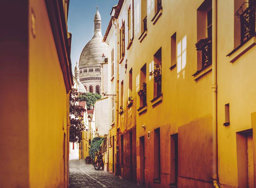Montmartre street with Sacré-Cœur dome and yellow buildings in Paris, France