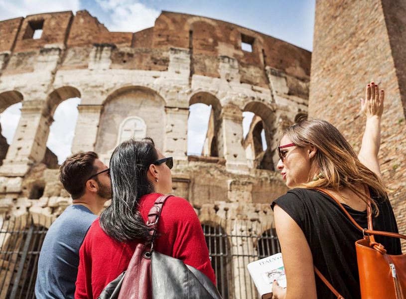 Tour group standing near Colosseum in Rome with guide pointing at ancient stone arches