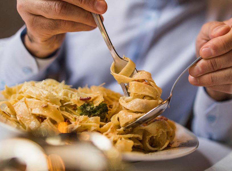 Close-up of hands twirling tagliatelle pasta with fork and spoon on white plate