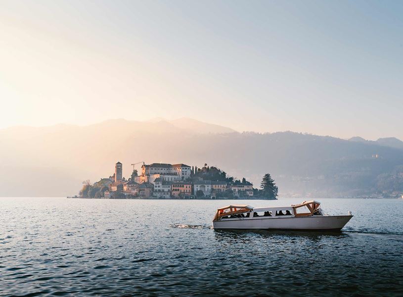 Boat cruising on Lake Orta with scenic island and mountains at sunset