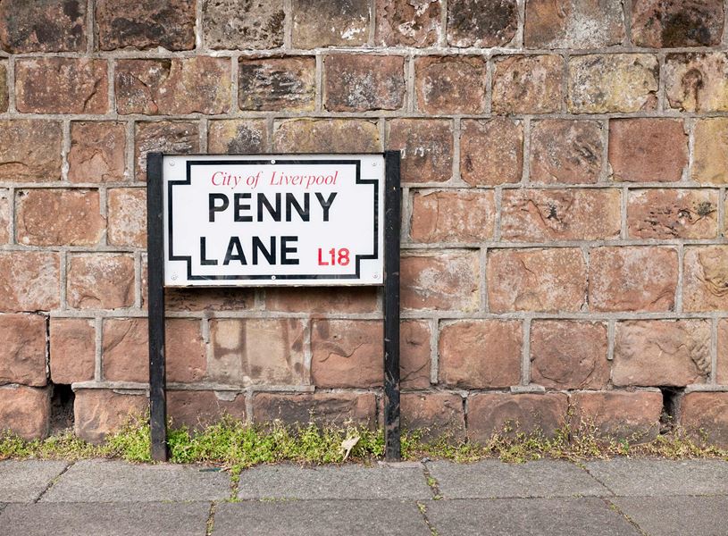 Penny Lane street sign mounted on black posts by brick wall in Liverpool, England