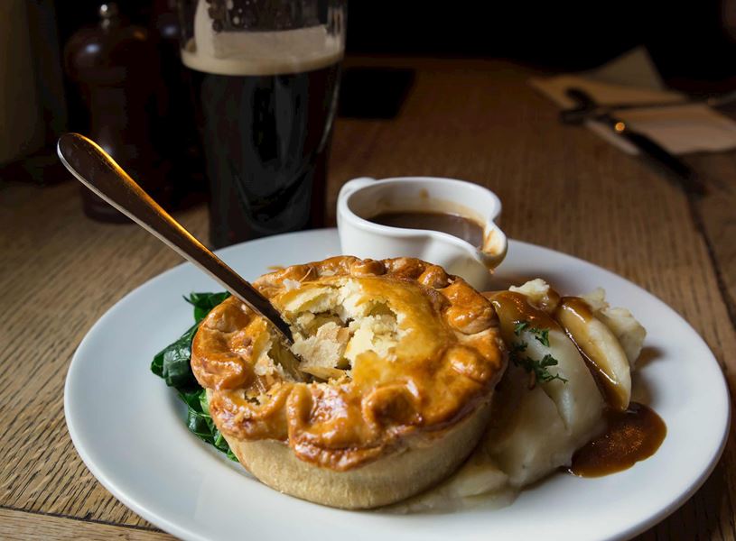 Savoury pie with mashed potatoes, gravy and greens on plate