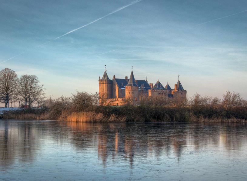 Muiderslot Castle reflected in calm water under blue sky