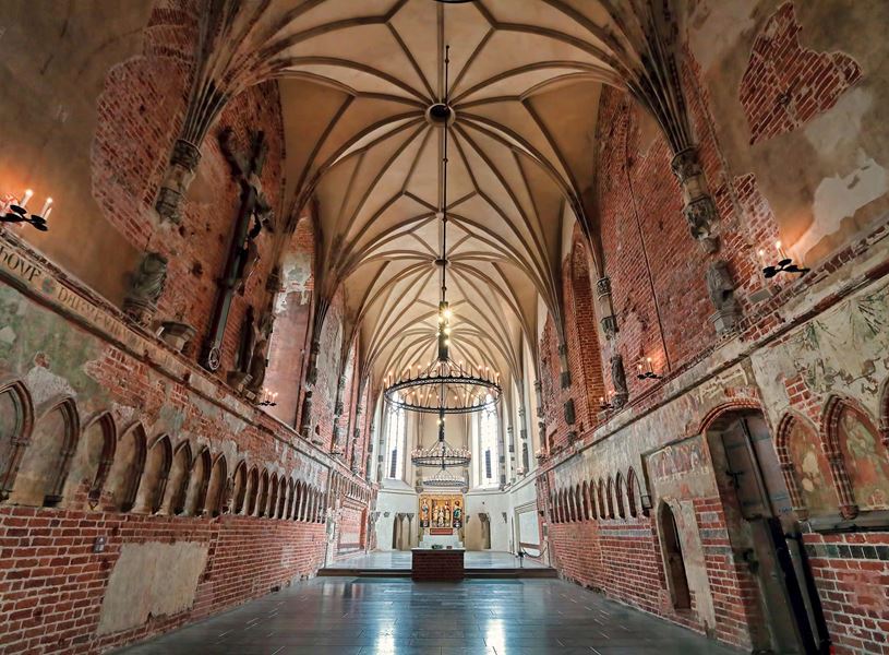 Gothic hall inside Malbork Castle with vaulted ceiling, brick walls and medieval chandeliers