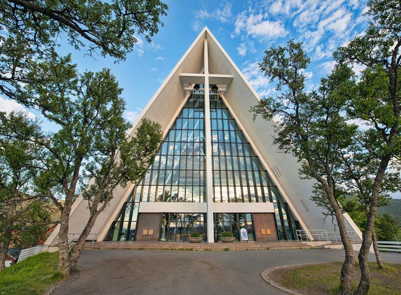 Arctic Cathedral with triangular architecture and glass facade framed by trees in Tromsø
