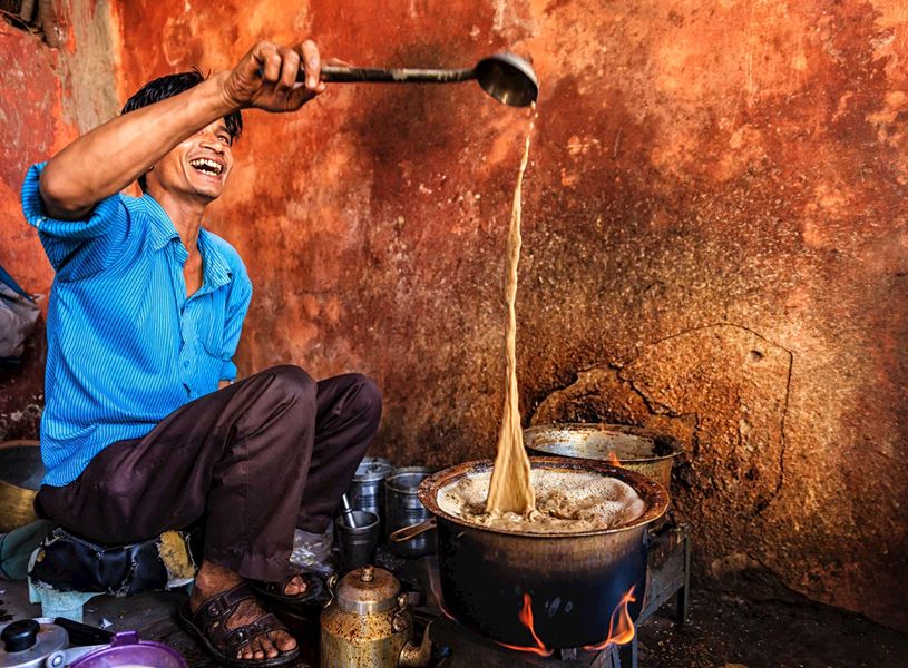 Smiling tea vendor pouring hot chai from a ladle at a local market in Jaipur, India