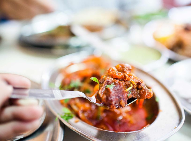Human hand picking mutton masala from a plate with a spoon, Kochi, India