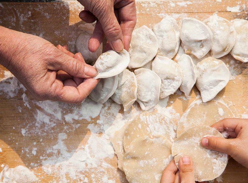 Two pairs of hands making dumplings on floury surface, Xi’an, China