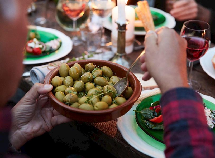 Close-up of a bowl of green olives being served with wine glasses and plates of food