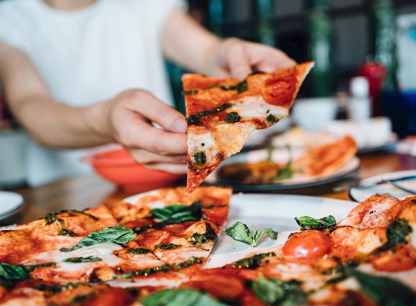 Hand holding slice of Margherita pizza with basil and cherry tomatoes 