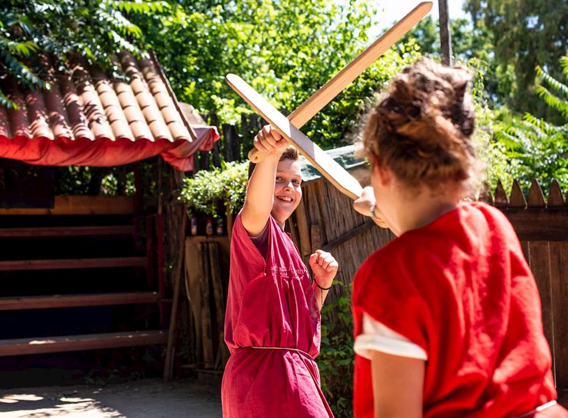 Two children reenacting Roman sword fight with wooden swords outdoors