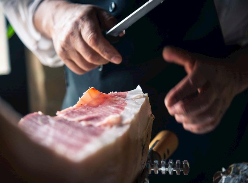Close-up of hands slicing Parma ham with knife on stand