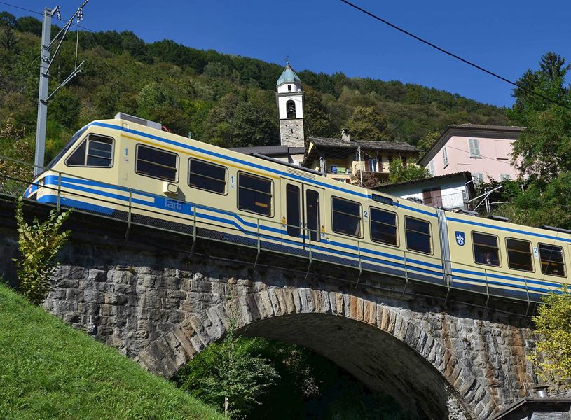 Centovalli train crossing stone bridge with alpine village in background