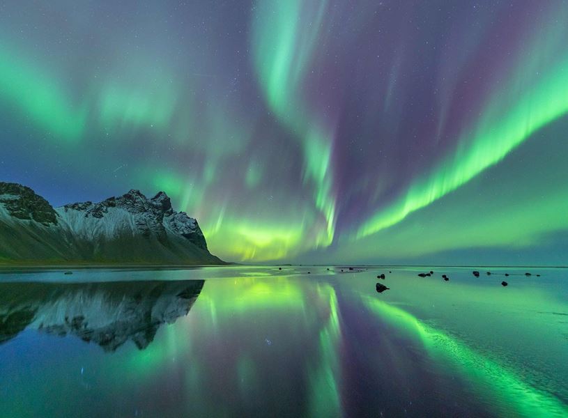 Northern Lights over snowy mountains reflected in Icelandic lake