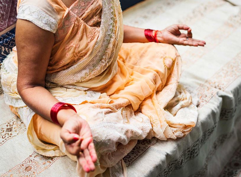 Woman in sari seated lotus style with hands forming Om gesture, Kumarakom, India