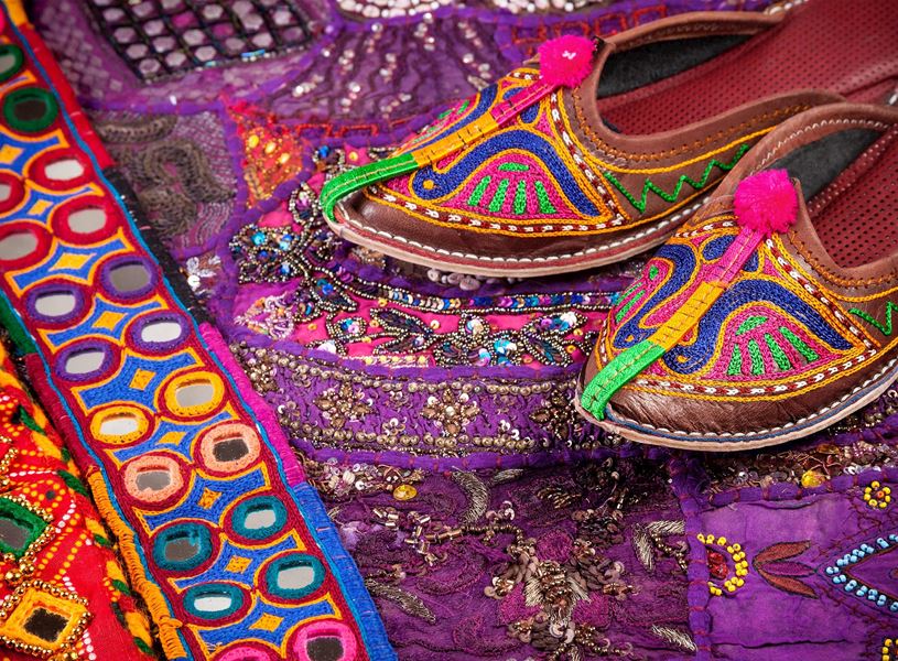 Colourful embroidered Indian shoes on vibrant decorative fabric background, Delhi, India