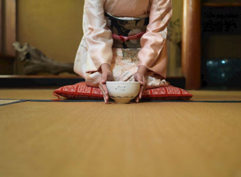 Person in traditional attire offering tea bowl at Ryokan, Kyoto, Japan