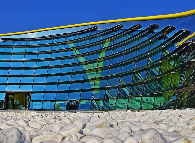 Modern glass facade of Enzo Ferrari Museum reflecting blue sky in Modena