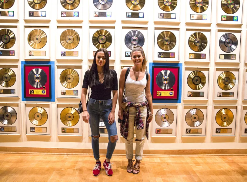 Two Travelers Standing By Record Wall At Country Music Hall of Fame In Nashville, USA