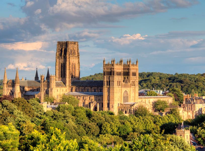 Durham Cathedral surrounded by greenery under partly cloudy sky in Durham, England
