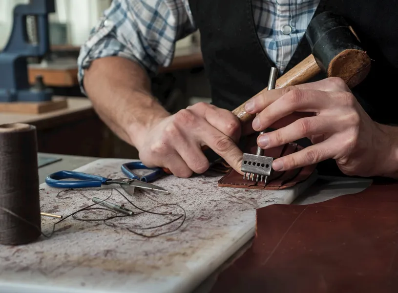 Craftsperson using leather stitching tool and mallet on a workbench