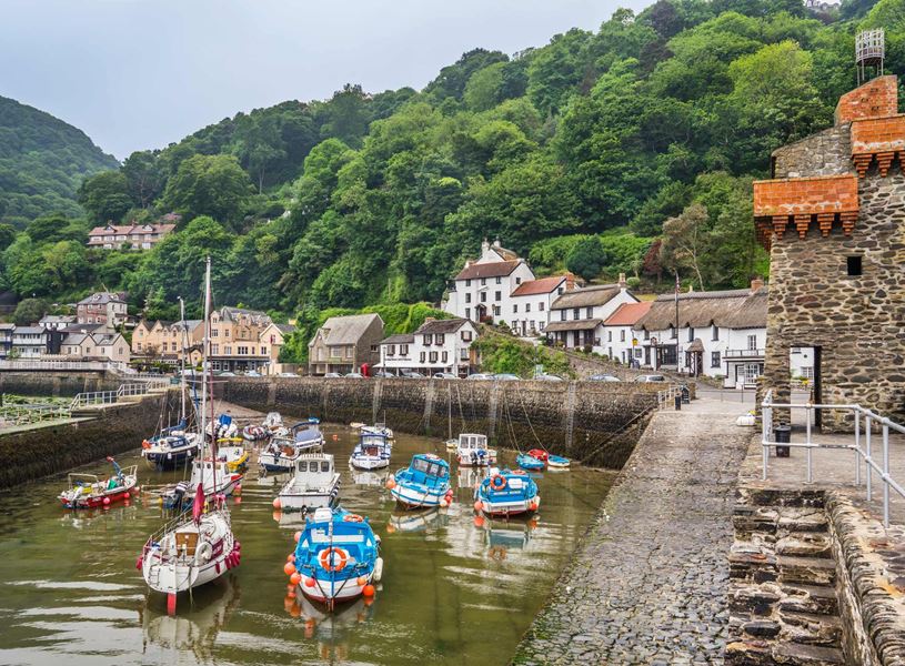 Lynmouth harbour with boats, cottages and green hills in Devon, England.