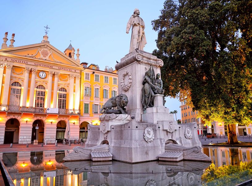 Illuminated Garibaldi Monument with fountain and historic building in Nice