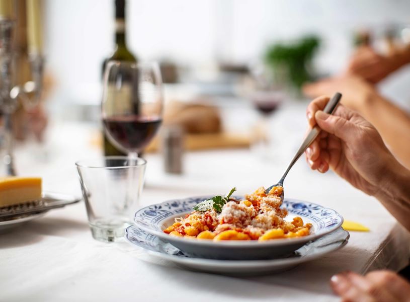 Hand holding fork over plate of pasta with tomato sauce and grated cheese