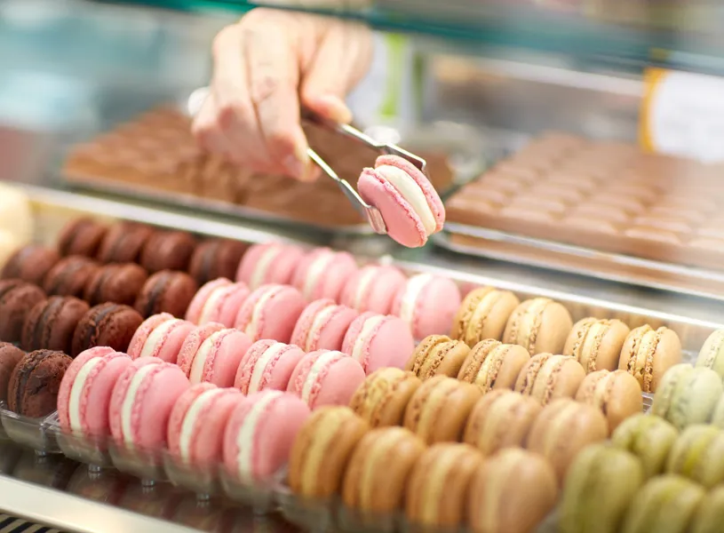 Tongs picking a pink macaron from assorted colourful macaron selection
