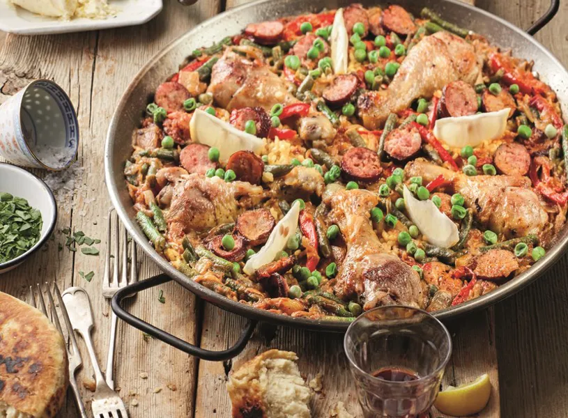 Paella with chicken, chorizo and vegetables on rustic table