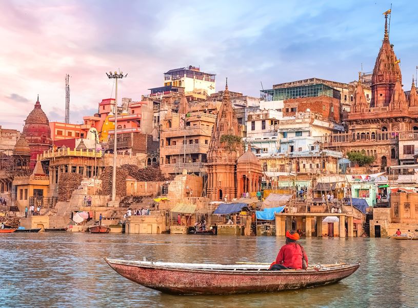 Hindu sadhu on Ganges boat overlooking cityscape at sunset, Varanasi, India
