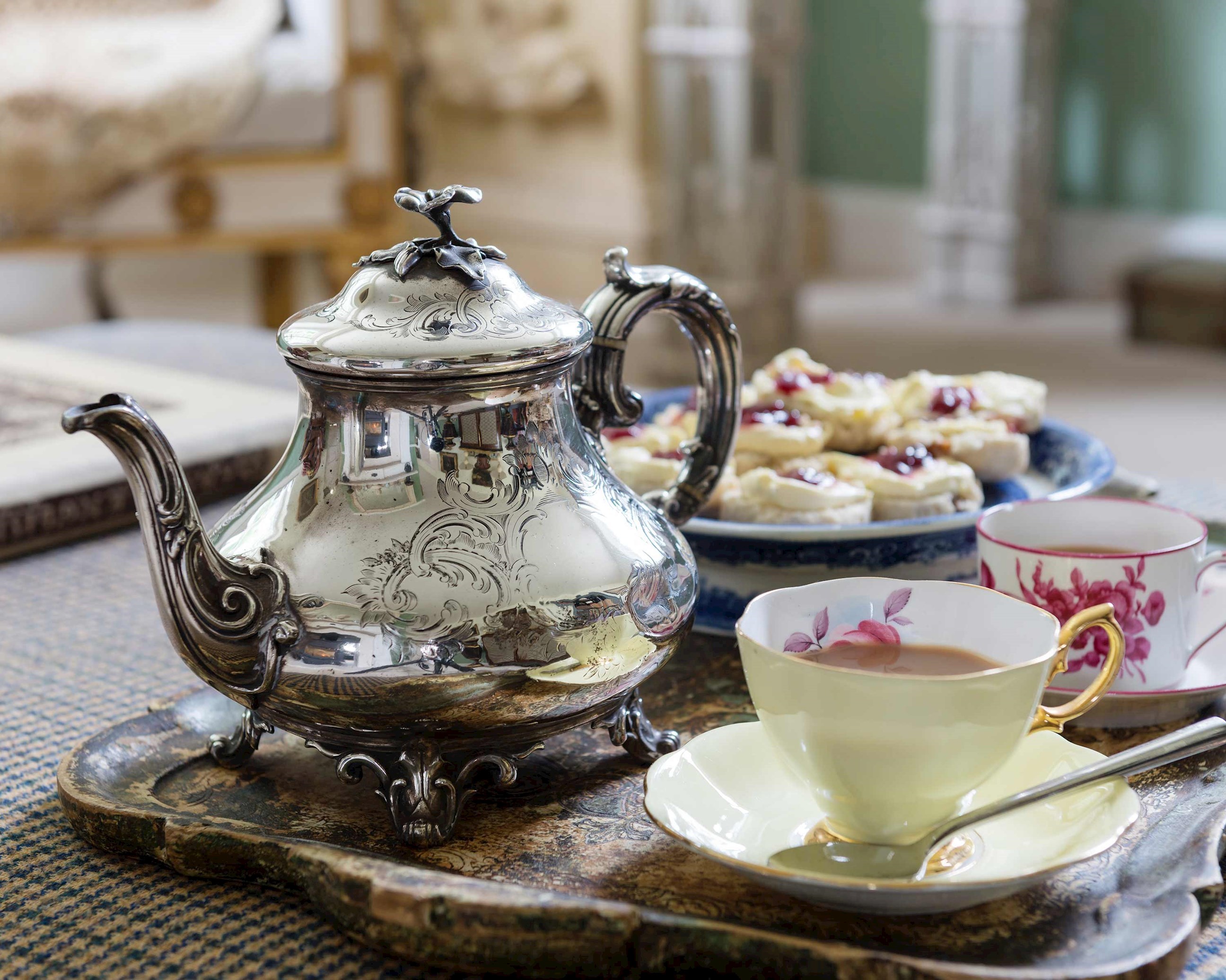 Silver teapot on tray with cups, saucers and scones for traditional English tea