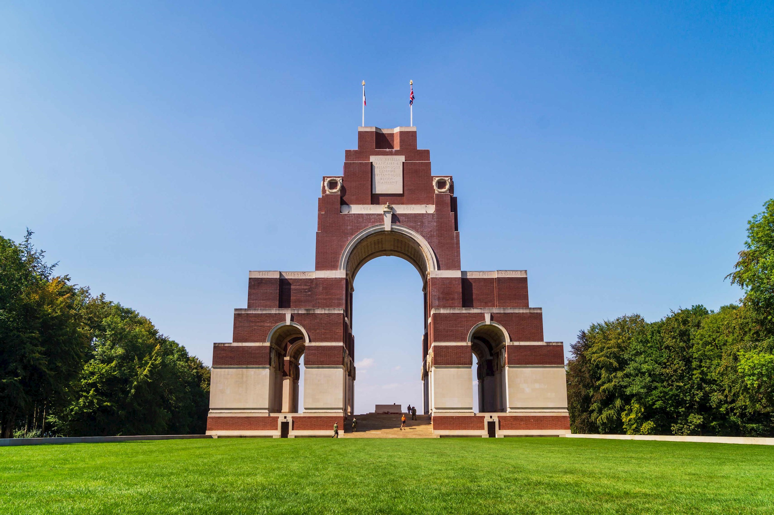 Thiepval Memorial arch with flags, trees, and clear blue sky
