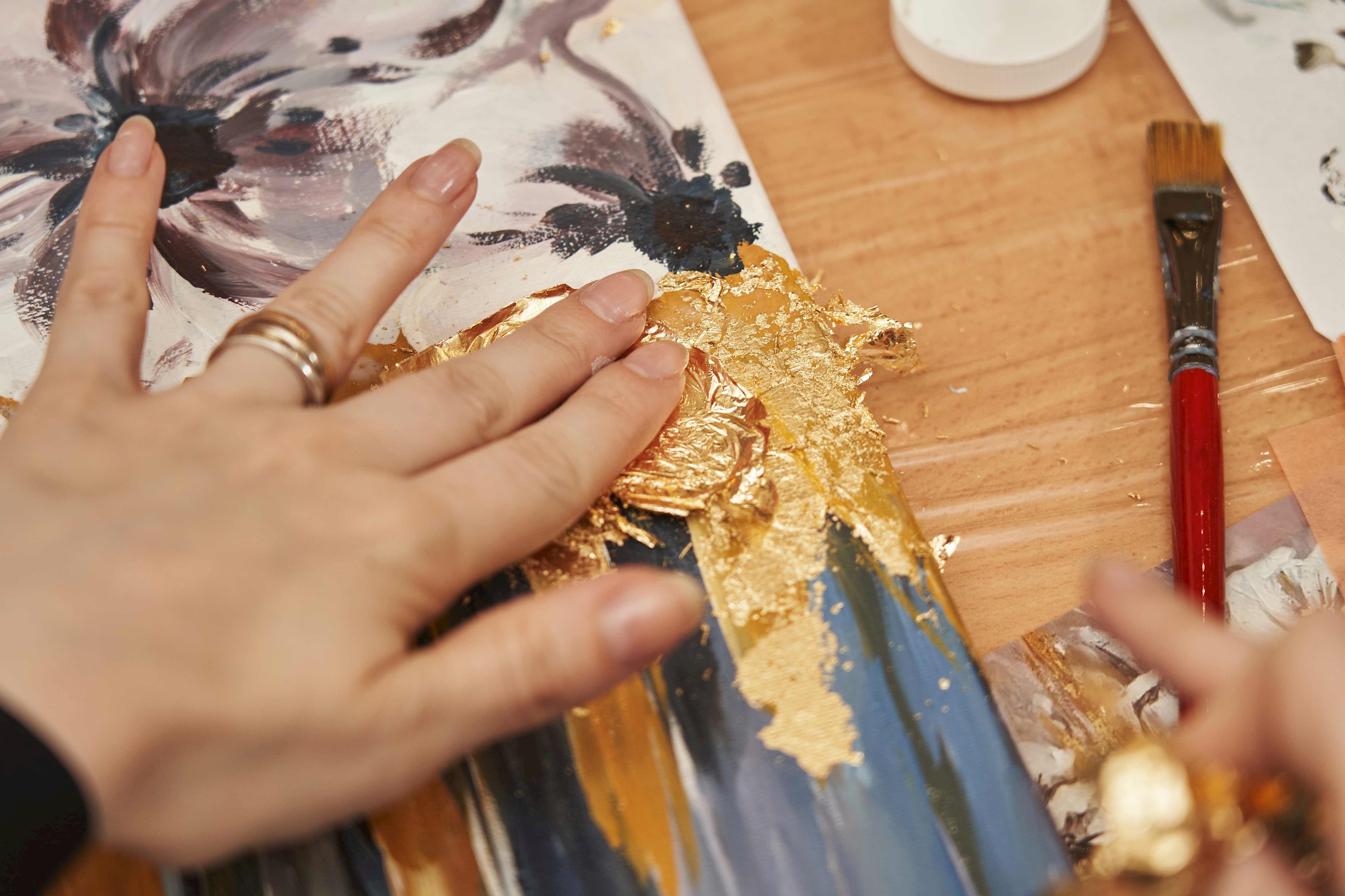 Hand applying gold leaf to a painted canvas with brush nearby, Kanazawa, Japan
