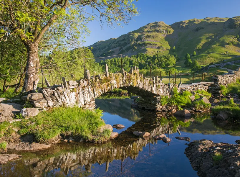 Stone footbridge over clear stream with green hills, Gretna Green, Scotland