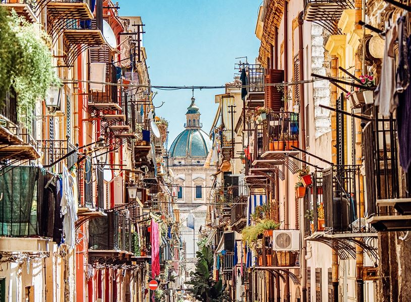 Narrow street lined with colourful balconies and view of dome in distance in Palermo 