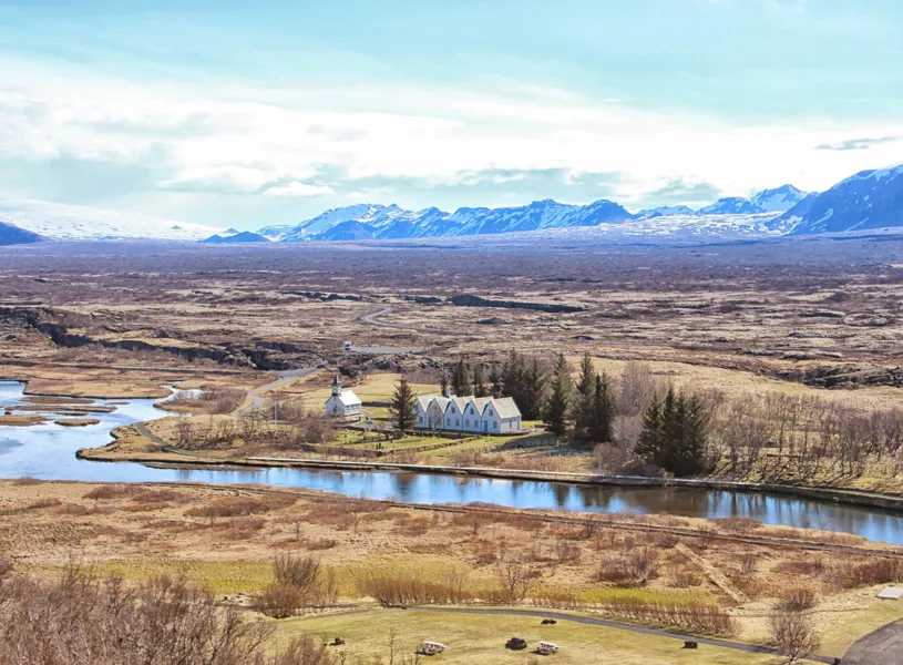 Thingvellir National Park with river, white buildings and snowy mountains