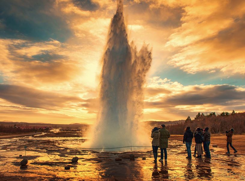 Strokkur Geyser erupting with onlookers and steam plume at sunset