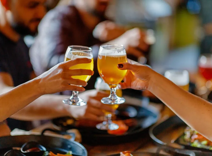 Close-up of hands clinking beer glasses at lively social gathering