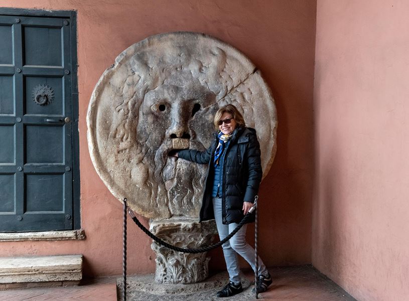Traveller standing beside Bocca della Verità stone sculpture with hand inside mouth